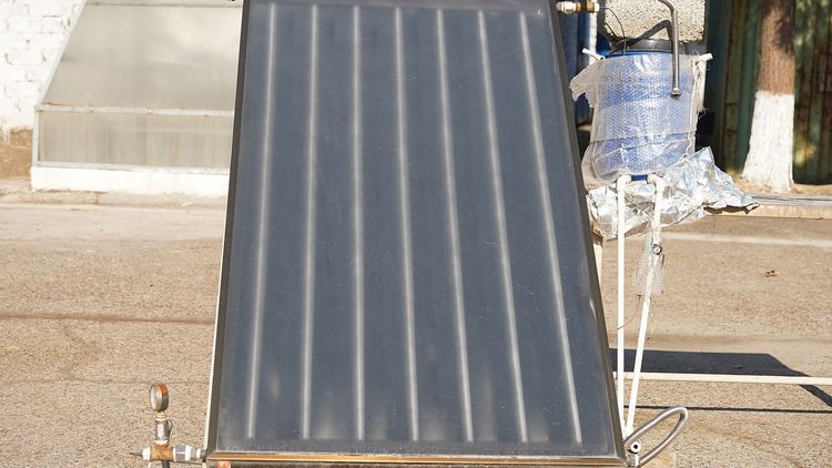 A flat-plate solar collector with visible absorber channels, mounted on a frame outdoors